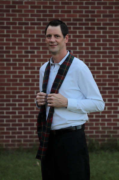 Man wearing a Quebec tartan red, green, and yellow plaid scarf in front of a brick wall