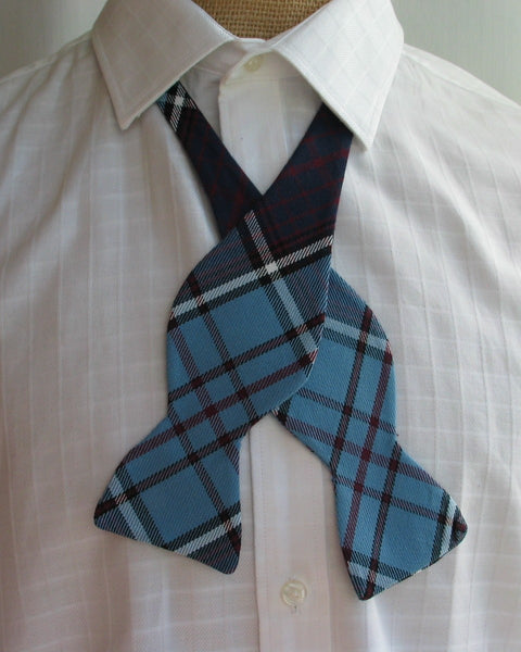 Blue plaid bow tie by Taylors Tartans on a white shirt against a neutral background