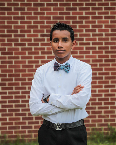 Person looking at camera in white shirt with a RCAF tartan bow tie and black pants in front of a brick wall