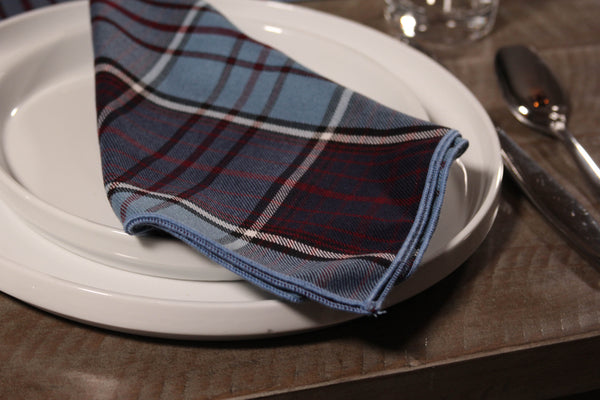 Close-up of an RCAF blue and maroon plaid napkin placed on a white plate atop a wooden table.