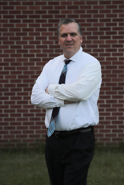 Man wearing a Royal Canadian Air Force tartan plaid necktie with a white shirt and black pants standing against a brick wall.