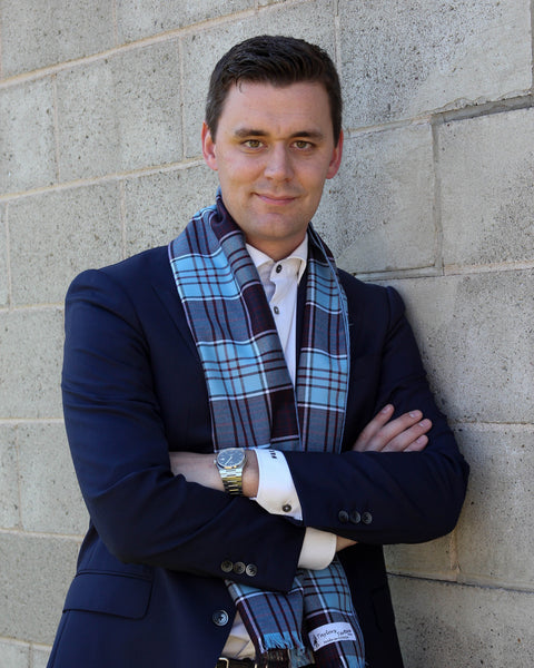 Man wearing a navy coat and plaid scarf against a stone wall