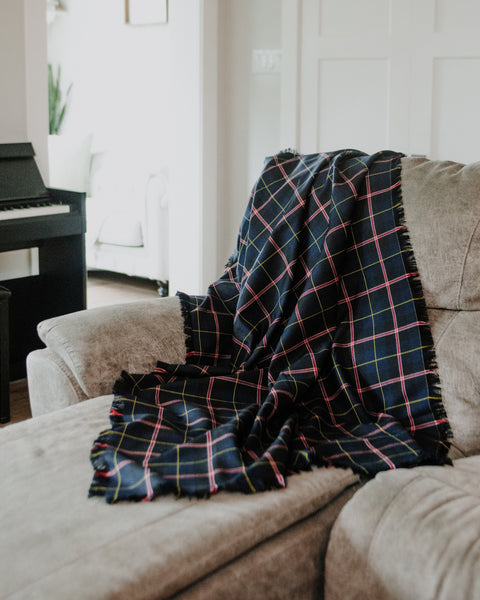 A dark navy plaid throw blanket with pink, yellow, and white lines is draped over a beige fabric sofa in a bright, modern living room.