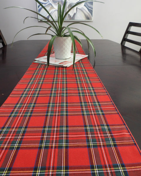 Red plaid table runner on a dark wooden table with a plant and books in the background.
