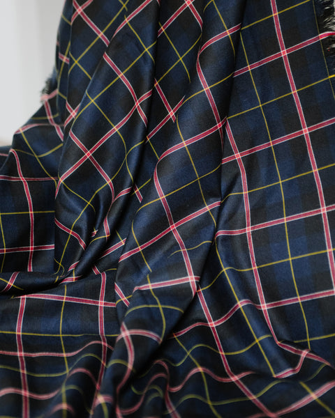 A close-up of Royal Canadian Navy tartan throw with a dark navy blue base and a plaid pattern formed by thin pink, yellow, and white intersecting lines.