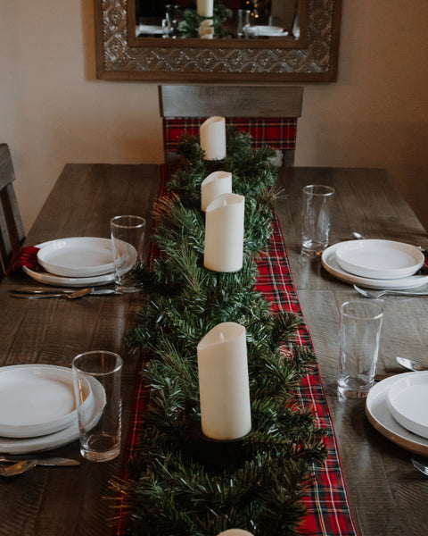 royal stewart tartan chair sash on a wooden chair behind a wooden table set with a matching table runner white candles and greenery 