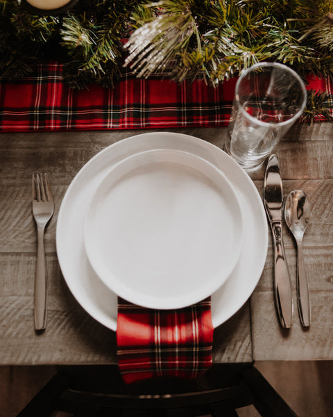 arial view of a wooden table with a white table setting and Royal Stewart tartan red green white and gold plaid napkins and matching table runner.