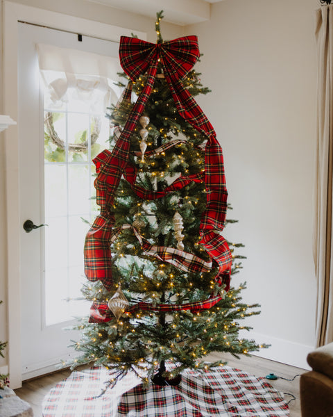 a royal stewart tartan christmas tree bow on the top of a prelit christmas tree with a white door in the background.