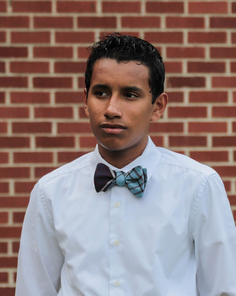 Man wearing a white shirt with blue and plum bow tie against a brick wall