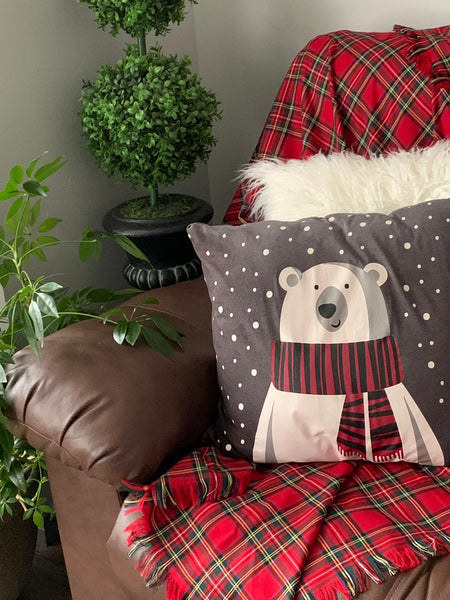 Red plaid Christmas blanket on a couch with decorative pillow and plants.