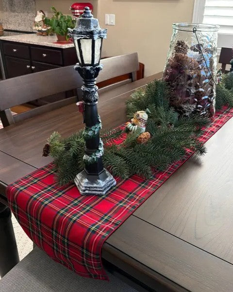 Dining table with a red plaid runner, decorative lamp, and Christmas decorations.