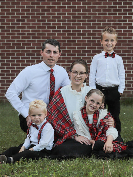 Family of five wear red plaid scarves and ties posing outdoors in front of a brick wall