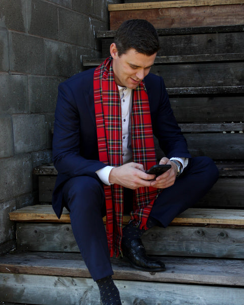 Man sitting on wooden steps wearing a blue suit and red plaid scarf, using a phone.