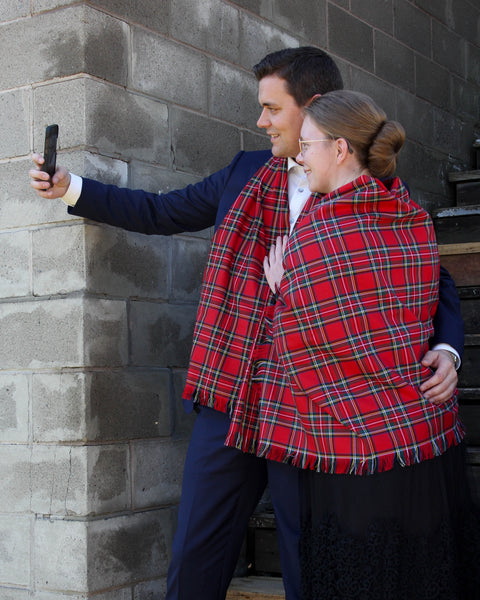 Two people taking a selfie against a brick wall, wearing red plaid scarves