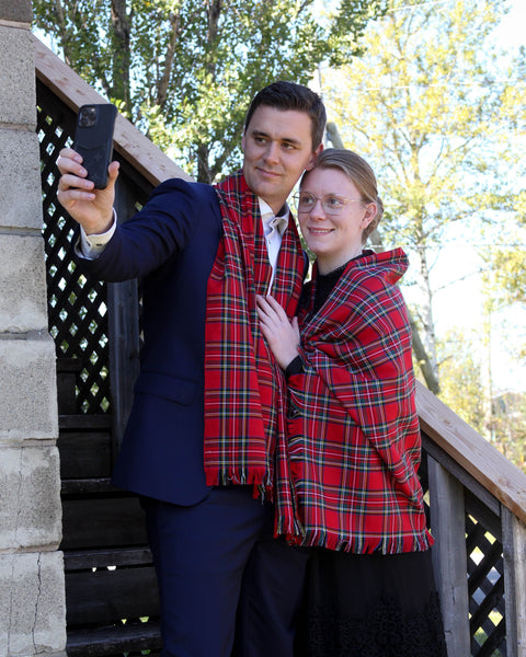 Two people wearing red plaid scarves taking a selfie on a wooden deck with trees in the background