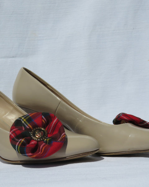 Beige high-heeled shoes with red plaid royal stewart tartan shoe clips on a light gray background