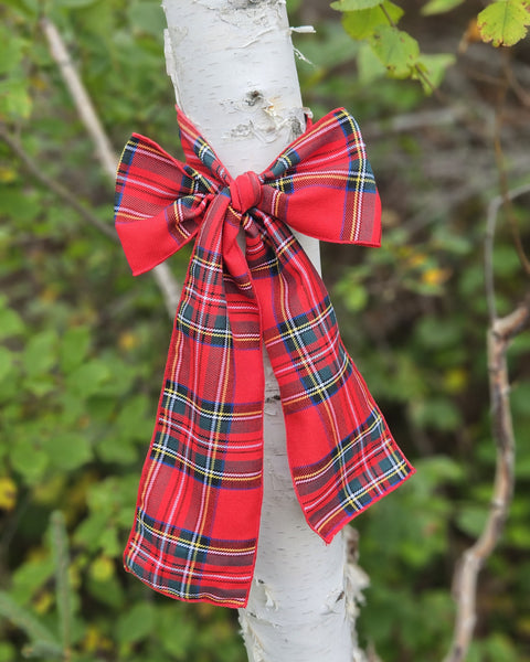 Red plaid bow tied around a tree branch with a natural green background