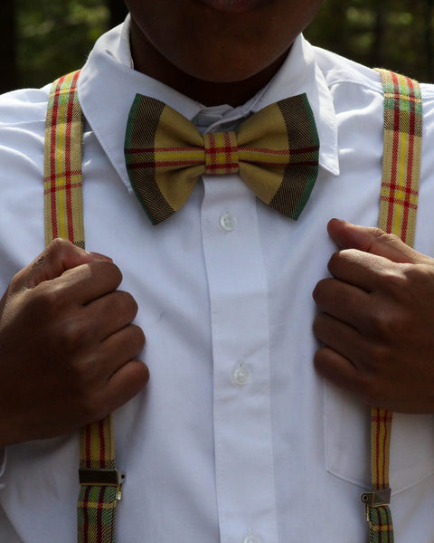 Person with darker skint wearing a white shirt with Saskatchewan plaid bow tie and suspenders.
