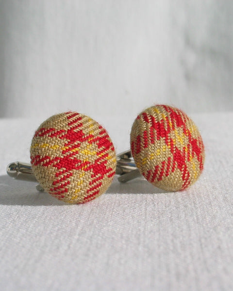 Pair of red and yellow plaid cufflinks on a white fabric background
