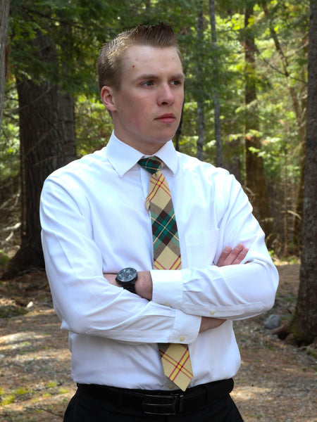 Man wearing a white shirt and plaid tie wiht arms crossed standing in a forest