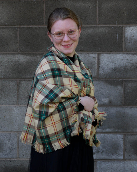 Person wearing a Saskatchewan plaid shawl against a brick wall