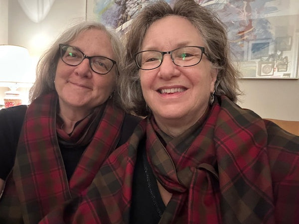 Two people wearing glasses and black shirts topped with a Canadian Maple leaf tartan plaid scarf, looking directly at the camera with a neutral expression.