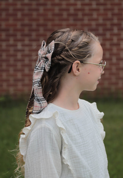 Girl with braided hair andtan hair bow in front of a brick wall