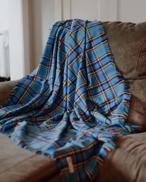 A blue plaid throw blanket with red, green, and yellow stripes draped over a brown fabric armchair in a home setting.