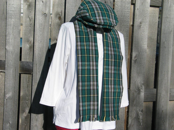 Green and gray plaid flat cap and scarf set on a mannequin wearing a white top, with a weathered wooden fence in the background.