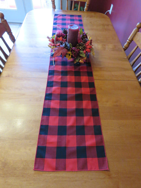 Aerial view of a black and red plaid table runner on a wooden table, topped with a fall-themed centerpiece.